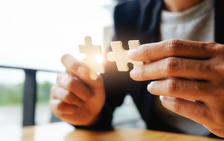 Hands connecting two jigsaw puzzle pieces, symbolizing partnership and trust.